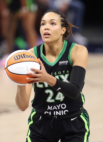 Napheesa Collier stands holding a orange and yellow basketball in her hands, preparing to take a free throw. 