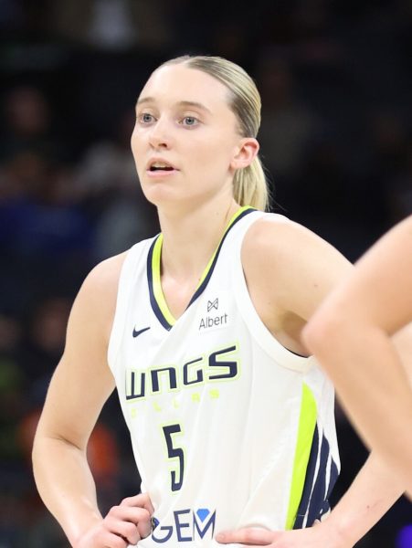 Paige Bueckers stands with hands on hips in a white Dallas Wings jersey.